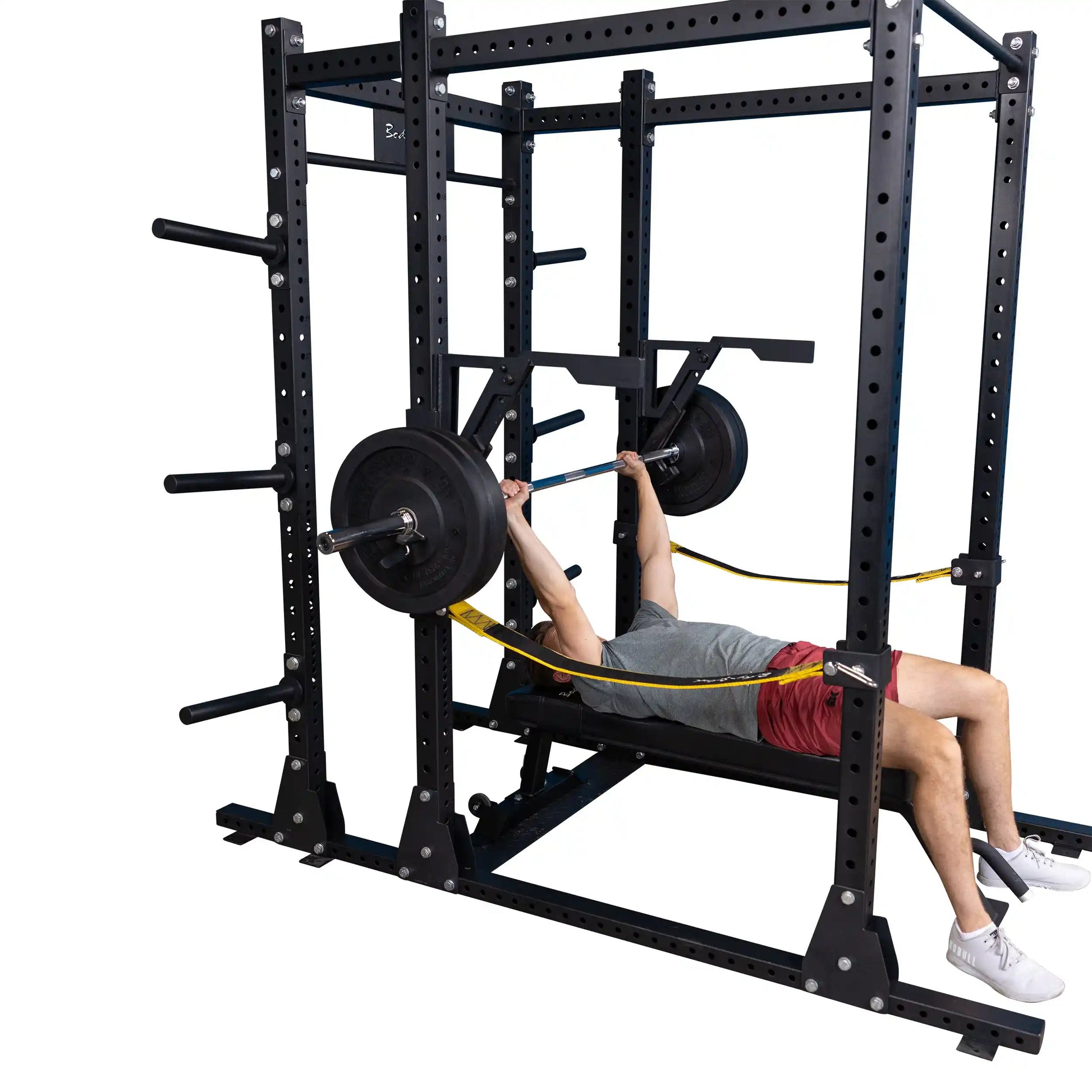 A person performing a bench press using the Body-Solid Pro Clubline Monolift Attachment SPRLFT, with weights on the barbell and resistance bands connected to the squat rack.