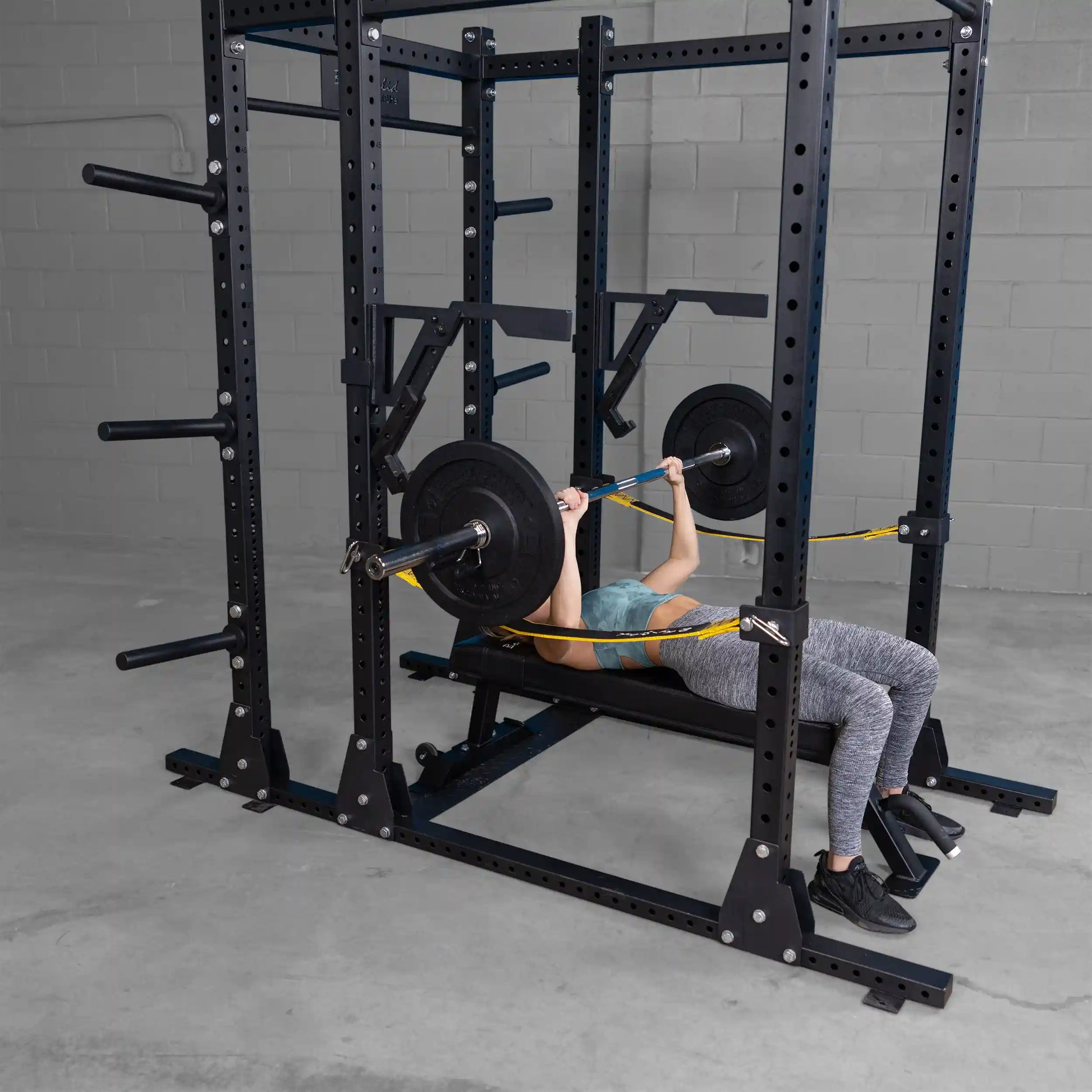 A person performing a bench press using the Body-Solid Pro Clubline Monolift Attachment SPRLFT, with a barbell and weights visible on both sides, inside a gym setting.