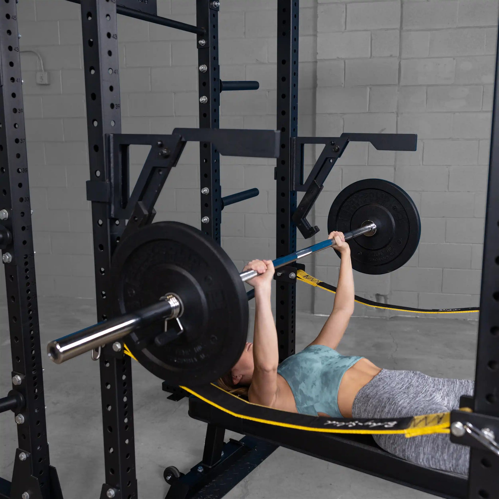 A person performing a bench press using the Body-Solid Pro Clubline Monolift Attachment SPRLFT, showcasing a weightlifting setup with a barbell and weights on a squat rack in a gym environment.