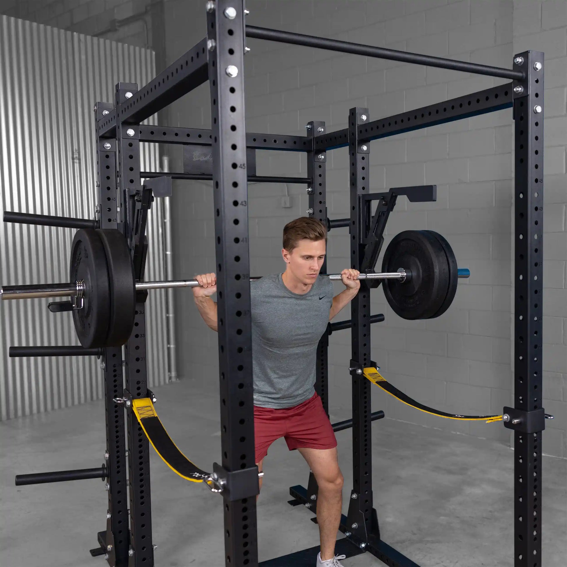 A man performing a squat with a barbell in a gym, using the Body-Solid Pro Clubline Monolift Attachment SPRLFT for support, within a squat rack setup.