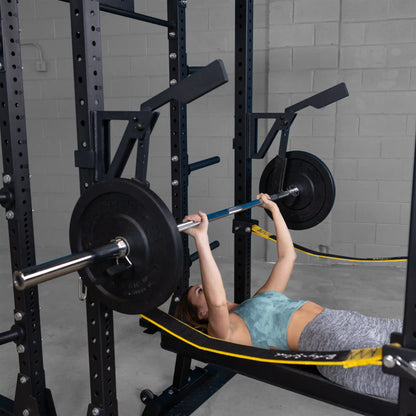 Woman performing a bench press using the Body-Solid Pro Clubline Monolift Attachment SPRLFT, with weight plates on either side of the barbell, in a gym setting.