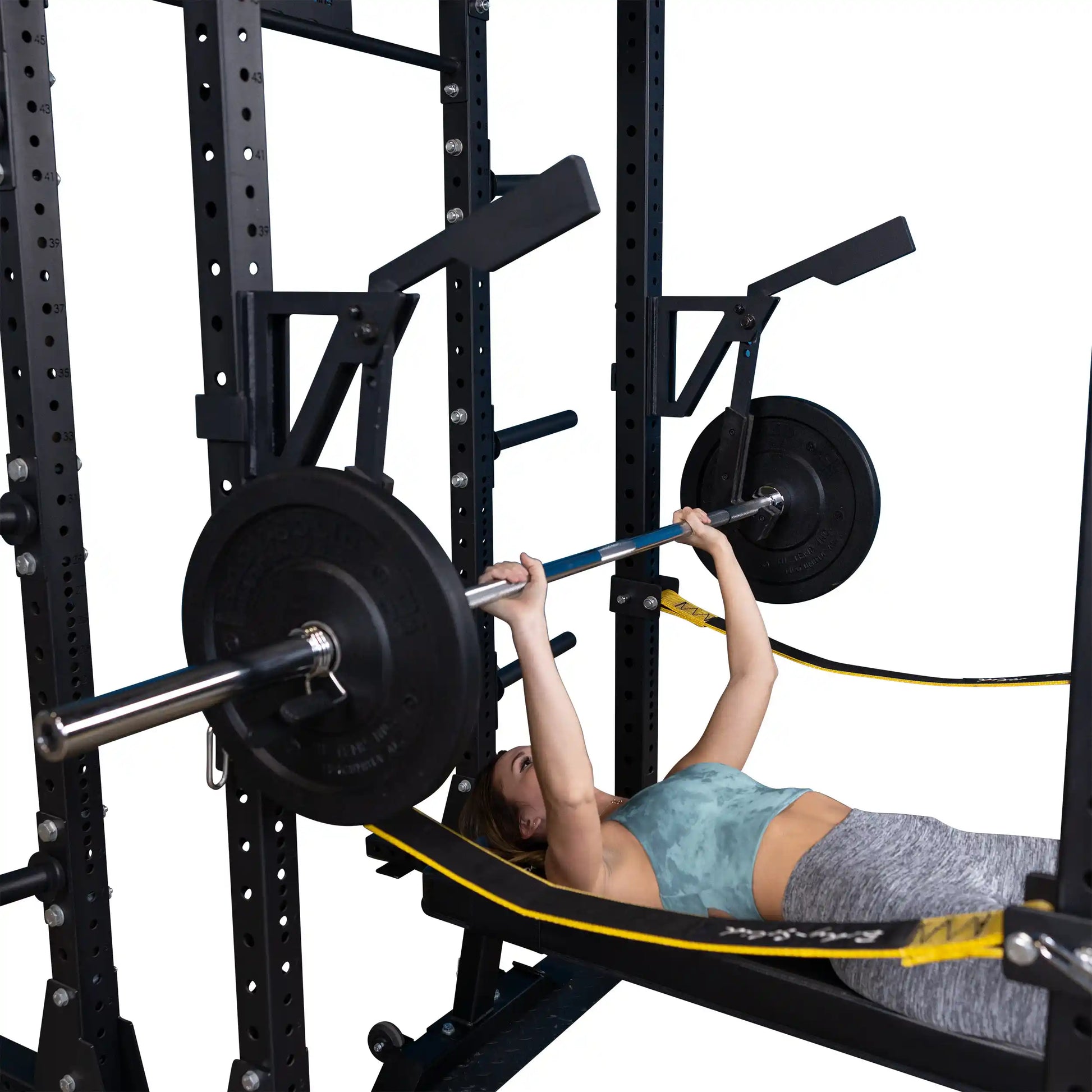 A person performing a bench press using the Body-Solid Pro Clubline Monolift Attachment SPRLFT, with a barbell loaded with weight plates and a sturdy power rack in the background.