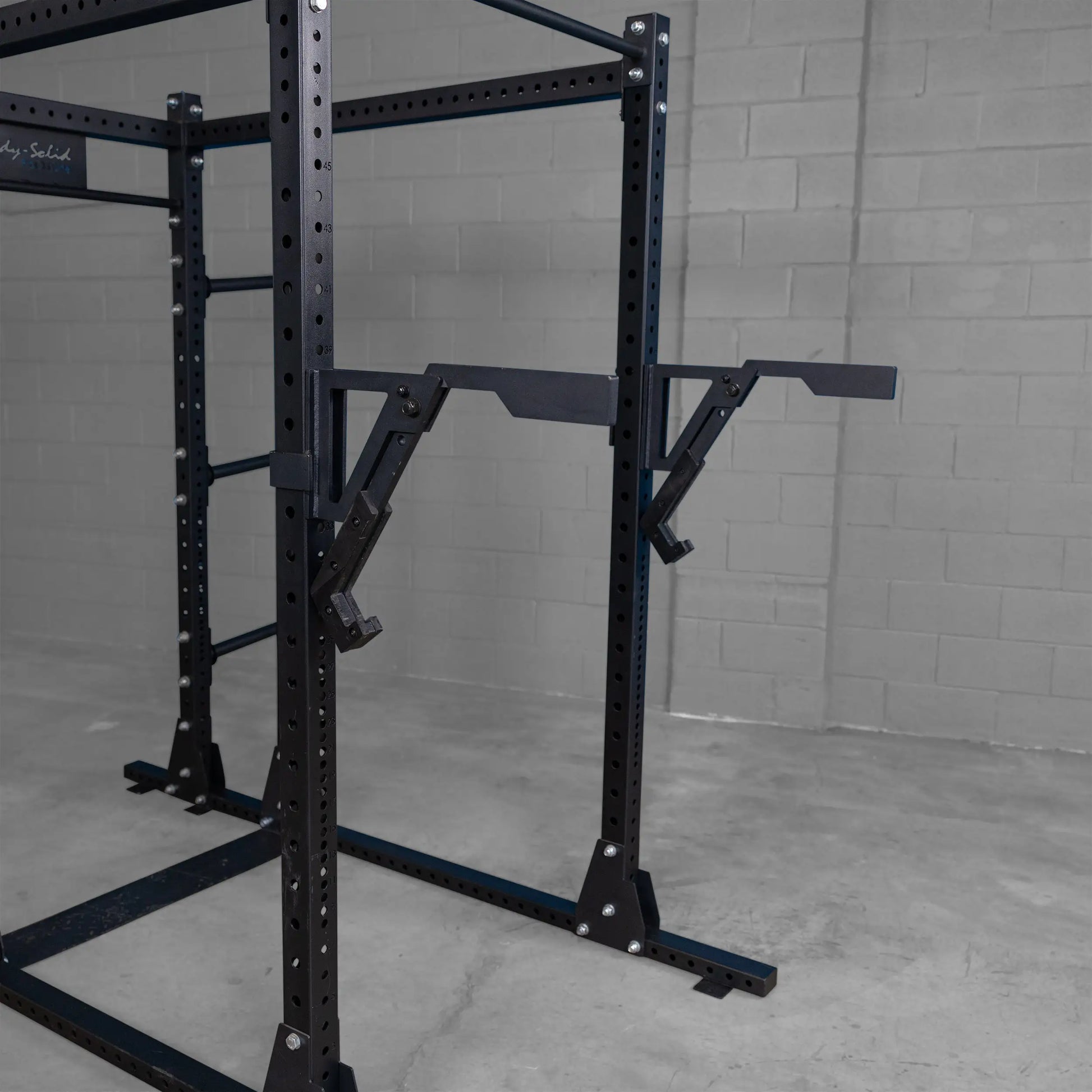 Close-up of the Body-Solid Pro Clubline Monolift Attachment SPRLFT attached to a squat rack, featuring adjustable arms and a sturdy black frame against a gray wall.