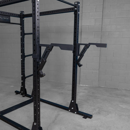 Close-up of the Body-Solid Pro Clubline Monolift Attachment SPRLFT attached to a squat rack, featuring adjustable arms and a sturdy black frame against a gray wall.