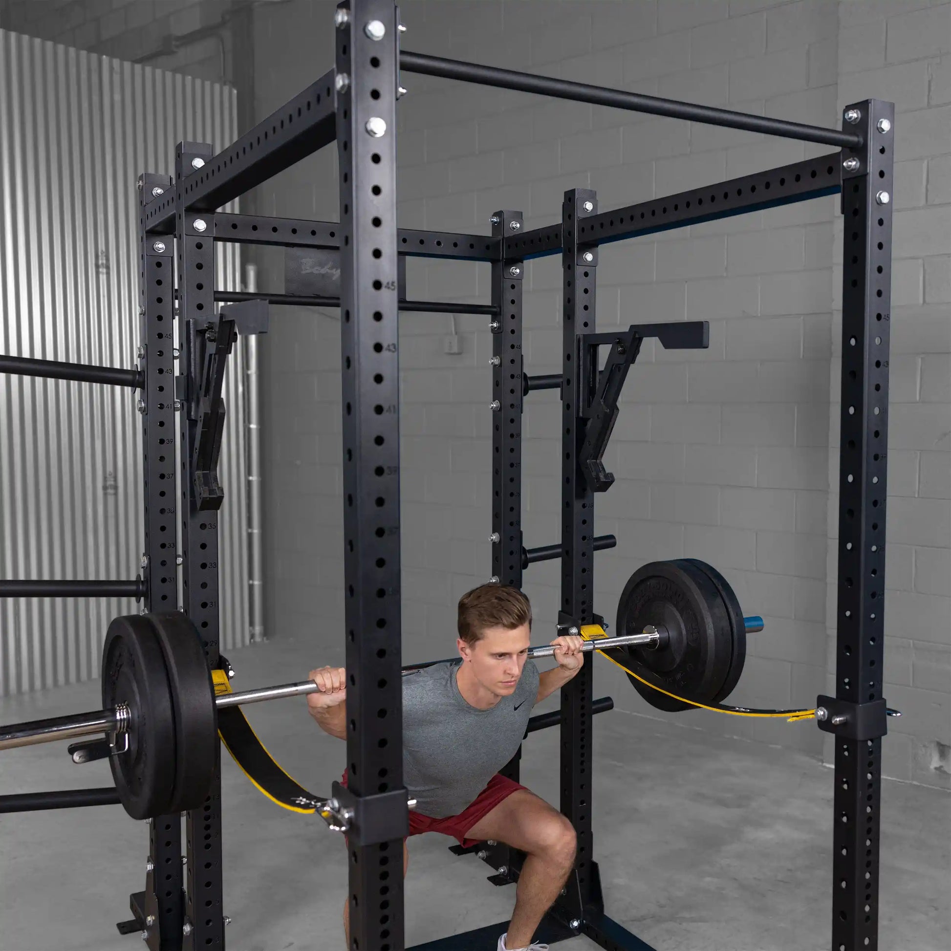 A person squatting with a barbell inside a gym using the Body-Solid Pro Clubline Monolift Attachment SPRLFT, showcasing a weightlifting setup with safety features.