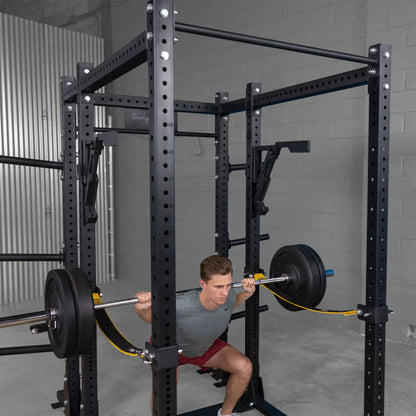 A person squatting with a barbell inside a gym using the Body-Solid Pro Clubline Monolift Attachment SPRLFT, showcasing a weightlifting setup with safety features.