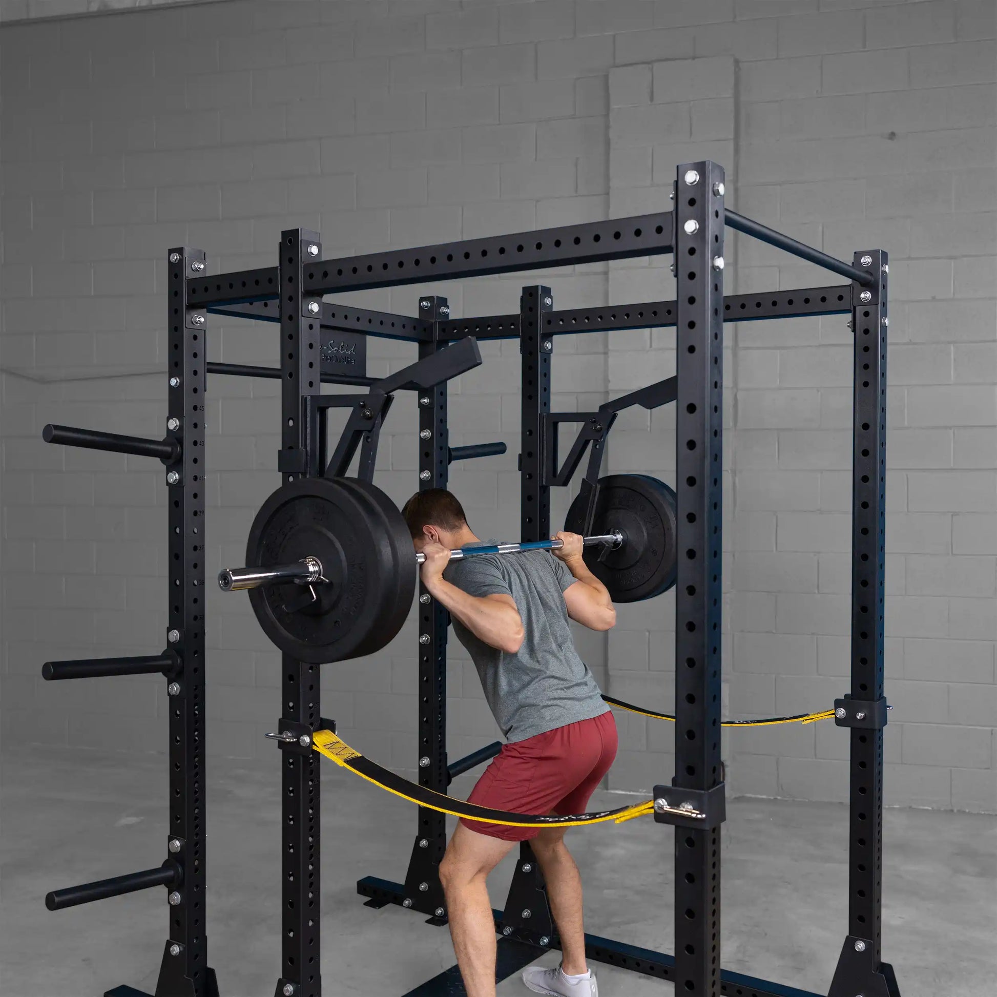 Person using the Body-Solid Pro Clubline Monolift Attachment SPRLFT for squats inside a weightlifting rack, with weights loaded on the barbell.
