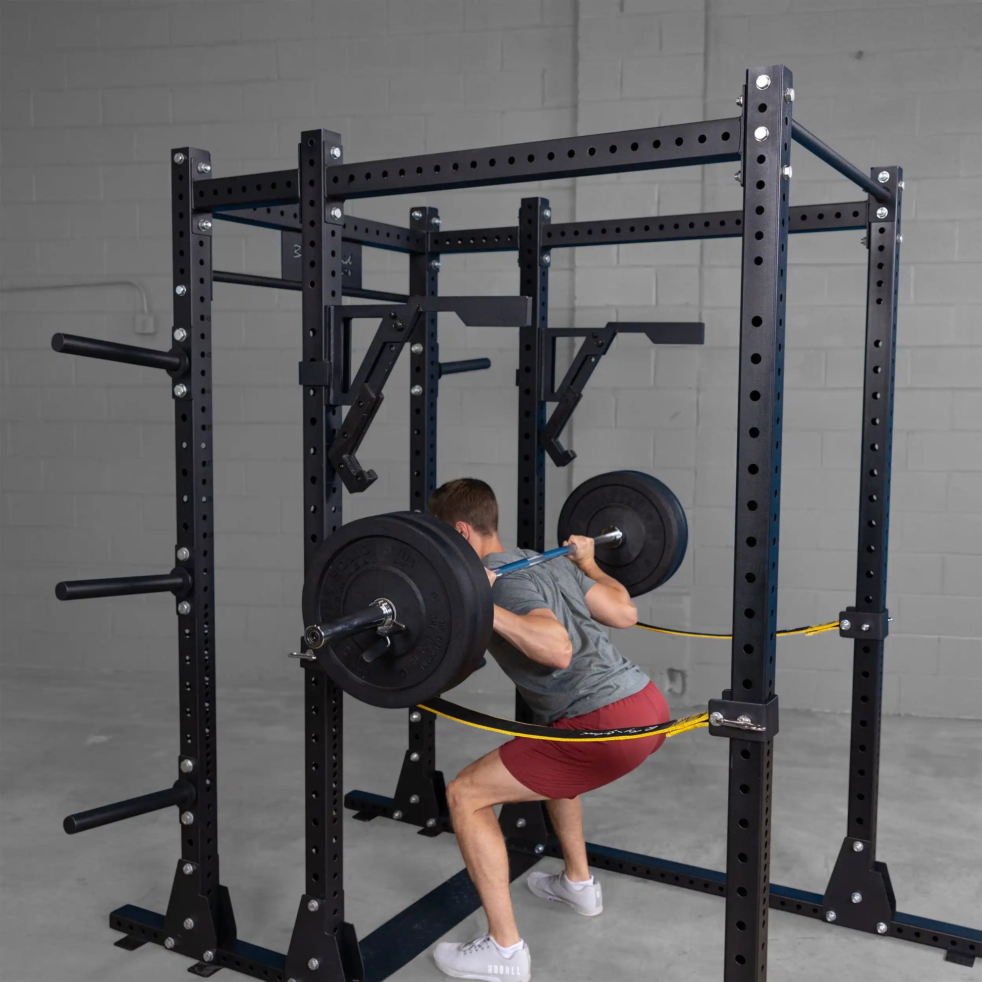 A person performs a squat with a barbell attached to the Body-Solid Pro Clubline Monolift Attachment SPRLFT, visible on a sturdy squat rack in a gym setting.