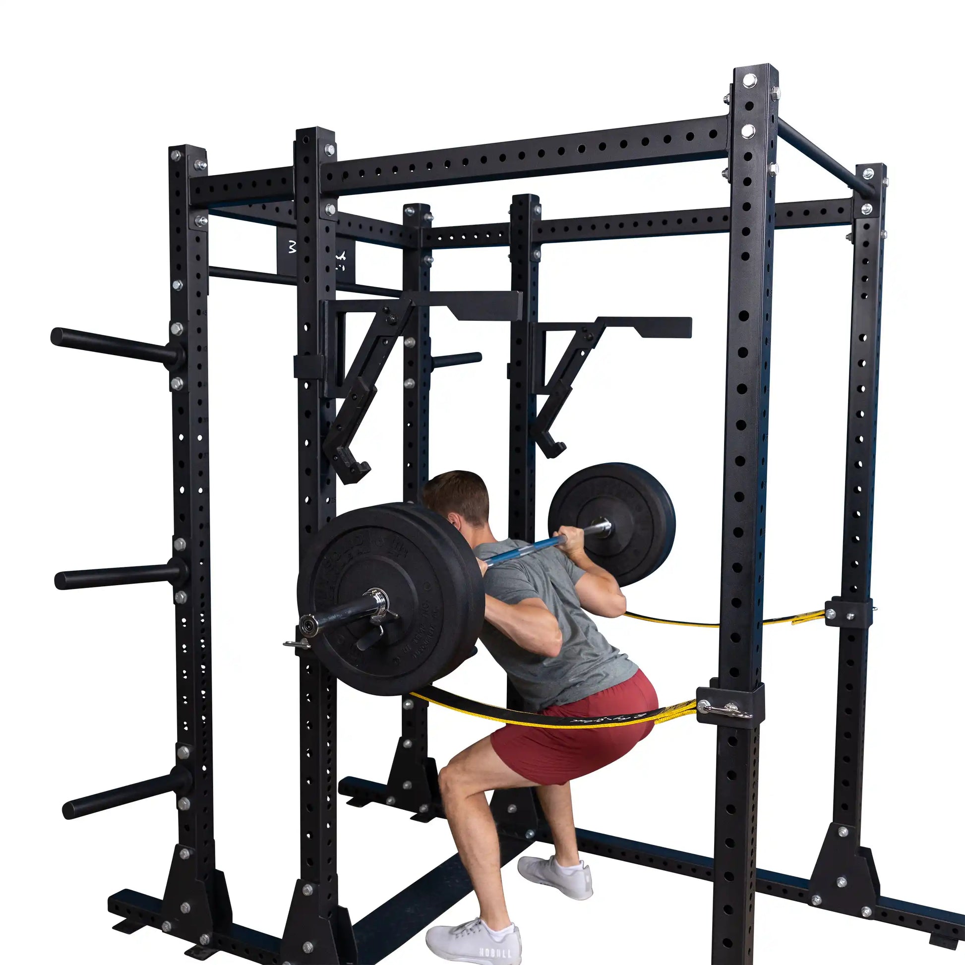 A person performing a squat using the Body-Solid Pro Clubline Monolift Attachment SPRLFT in a black squat rack, featuring multiple weight plates and a sturdy construction.