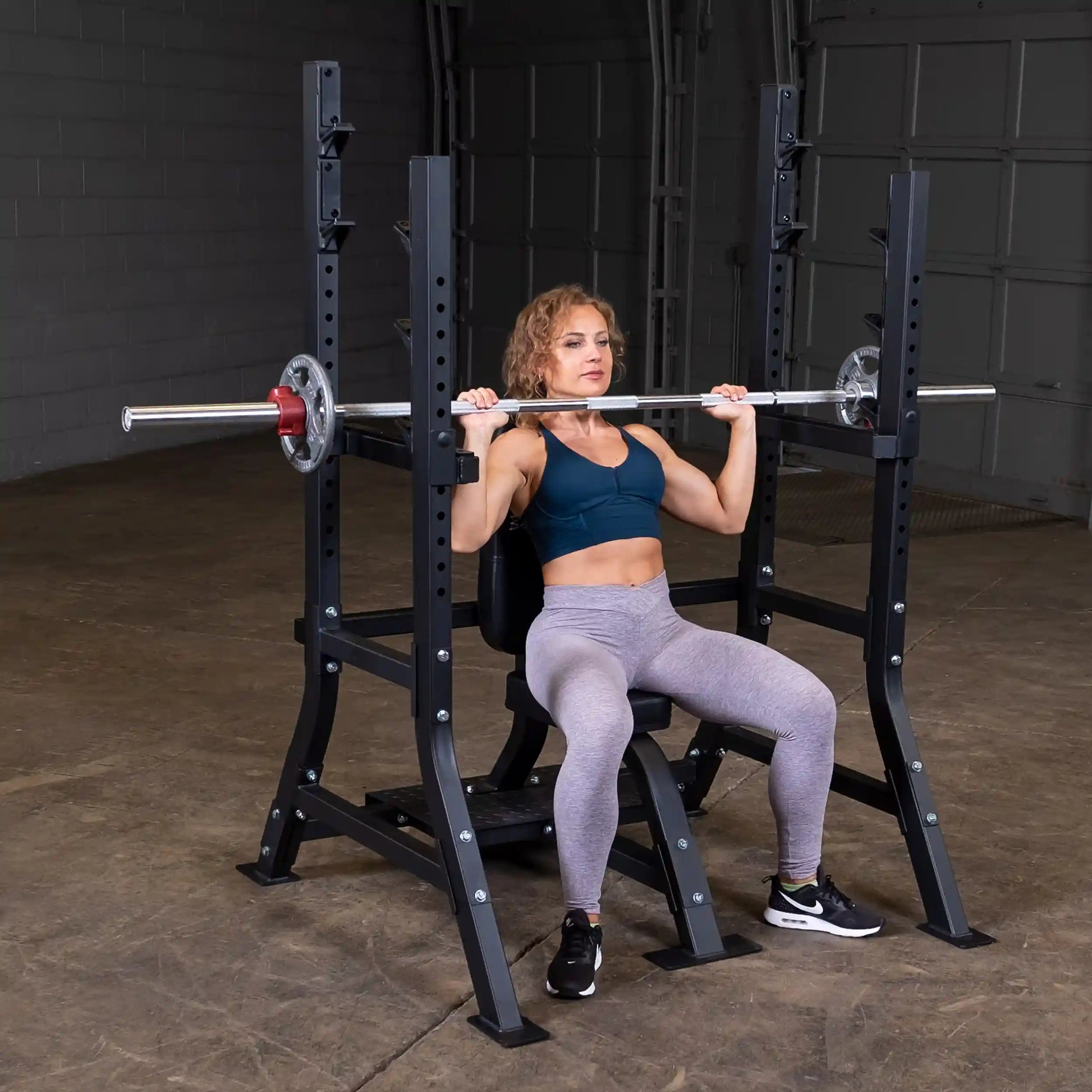 A woman performing a shoulder press exercise using the Body-Solid Pro Clubline Shoulder Olympic Bench SOSB250 in a gym setting.