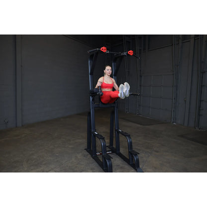 A woman in a red workout outfit demonstrates an exercise on the Body-Solid Pro Clubline Vertical Knee Raise SVKR1000, a fitness machine designed for core workouts, set in a gym environment.