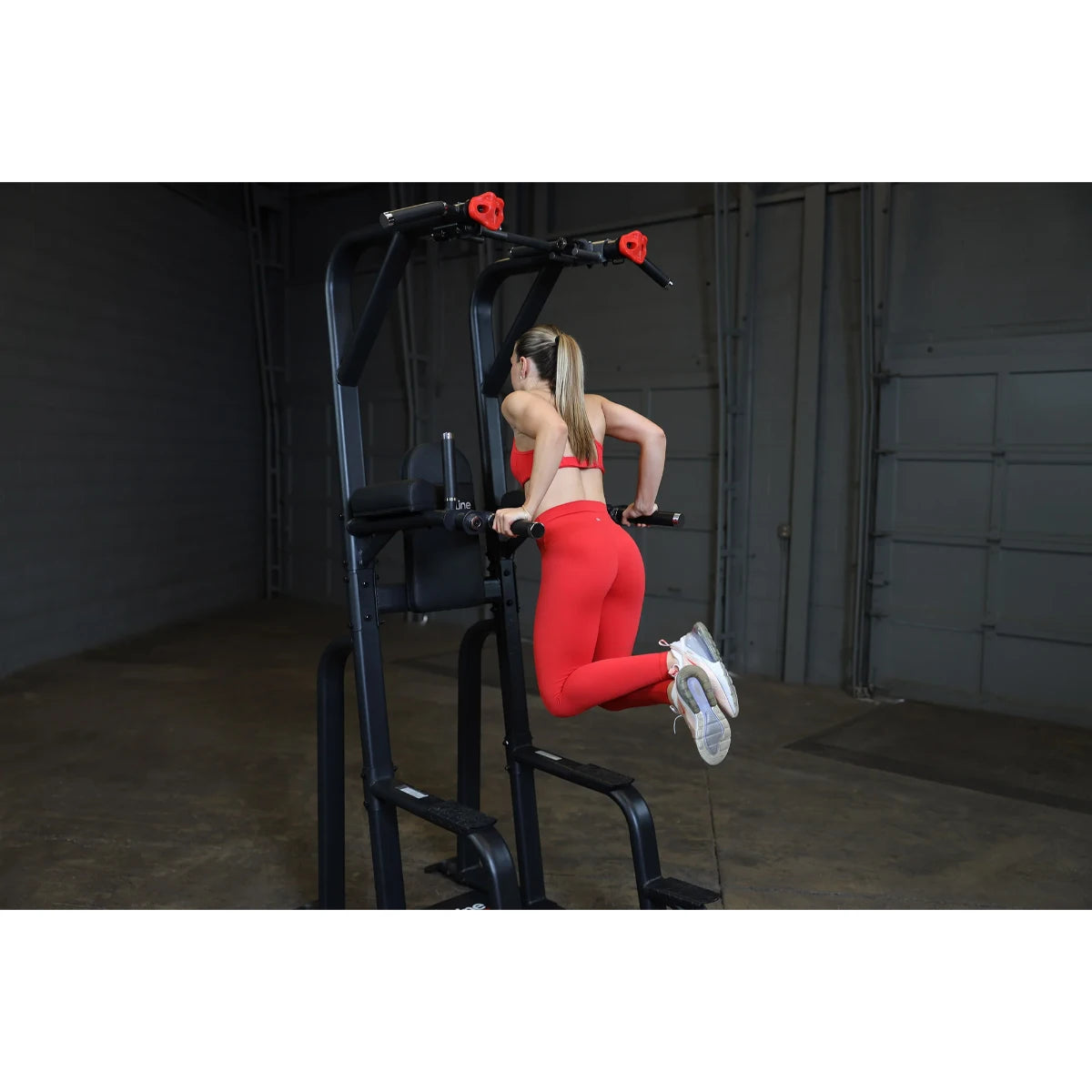 A person performing an exercise on the Body-Solid Pro Clubline Vertical Knee Raise SVKR1000, demonstrating proper form while using the equipment in a gym setting.