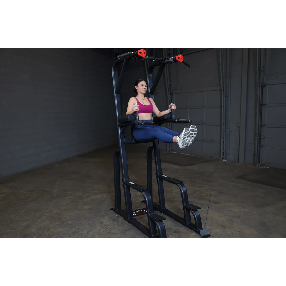 A woman demonstrating an exercise on the Body-Solid Pro Clubline Vertical Knee Raise SVKR1000, performing a knee raise in a gym setting.