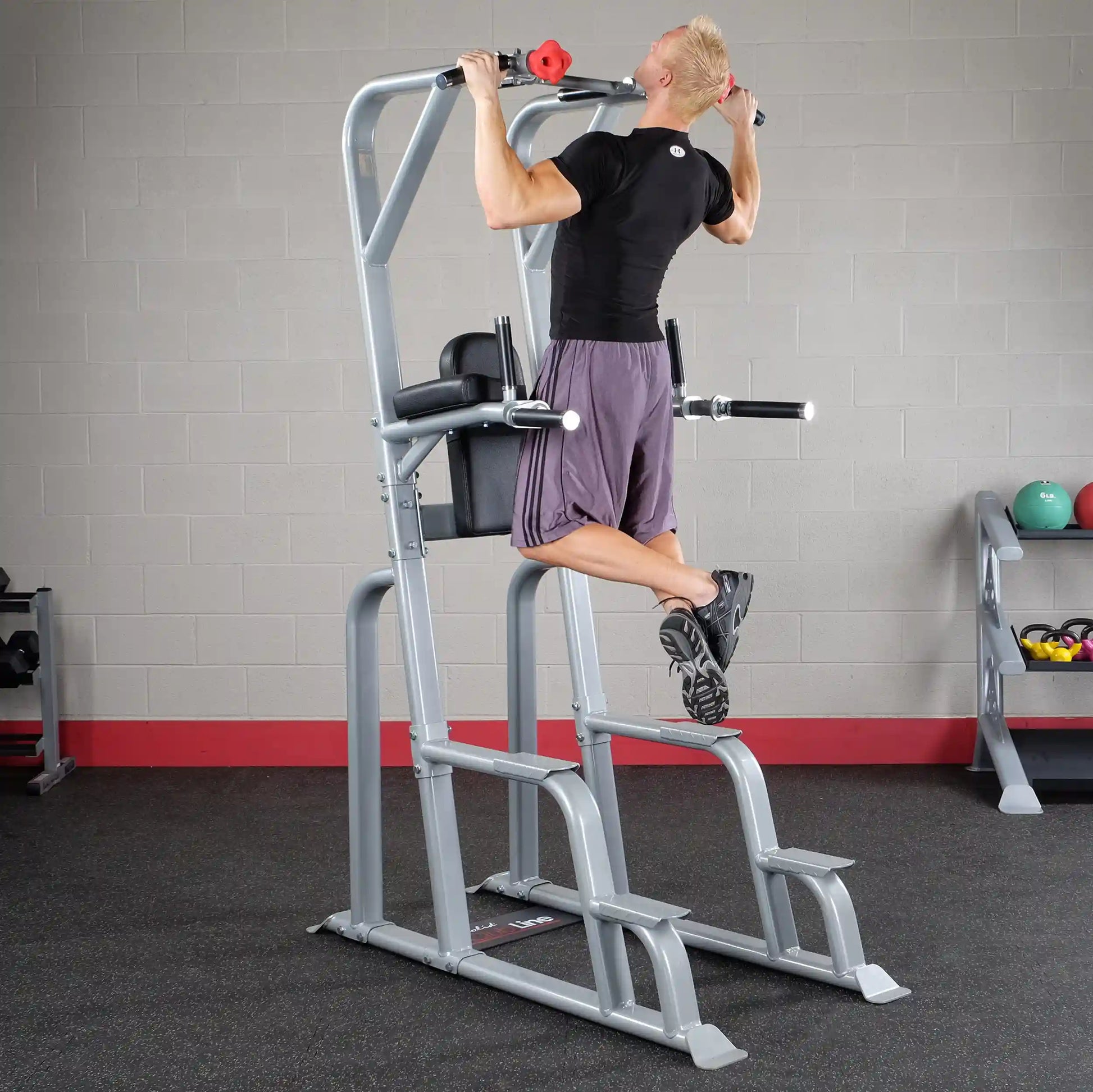 A person performing an exercise on the Body-Solid Pro Clubline Vertical Knee Raise SVKR1000, showcasing the equipment's design and functionality in a gym setting.