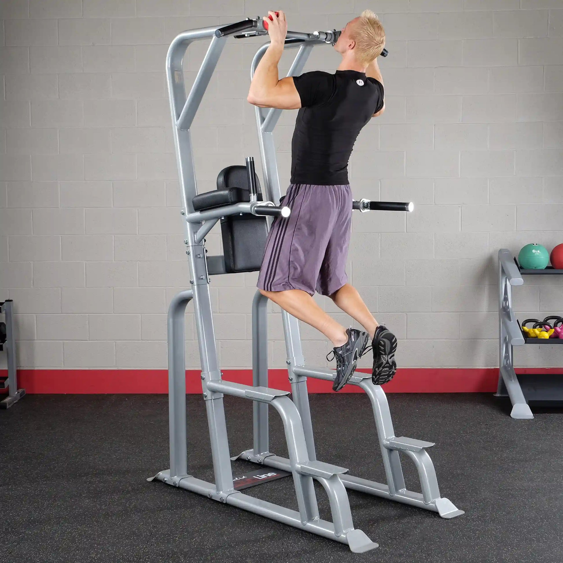 A person performing a pull-up on the Body-Solid Pro Clubline Vertical Knee Raise SVKR1000, showcasing the exercise equipment in a gym setting.