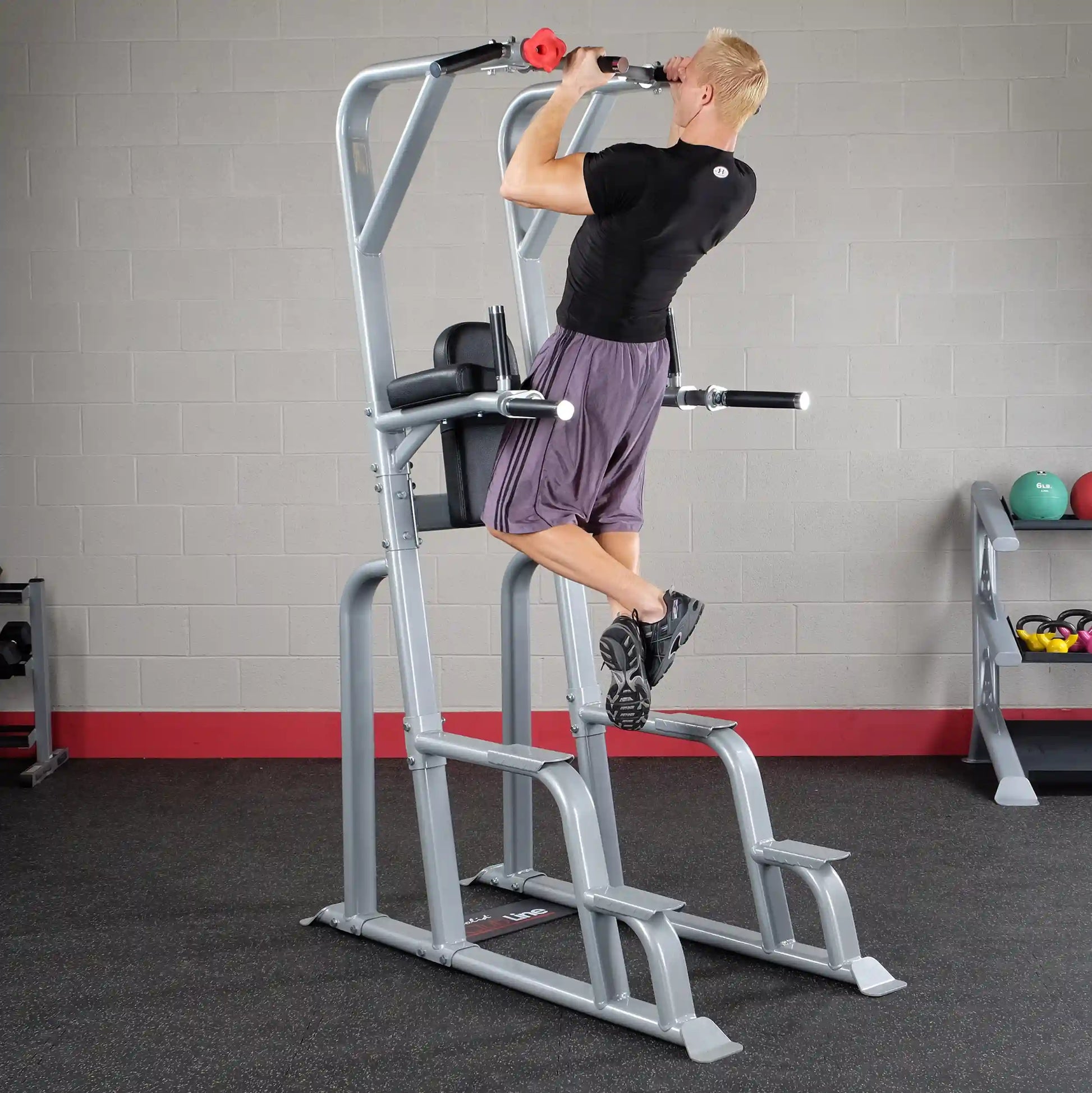 A person demonstrating an exercise on the Body-Solid Pro Clubline Vertical Knee Raise SVKR1000, performing a pull-up with feet elevated, in a gym setting.