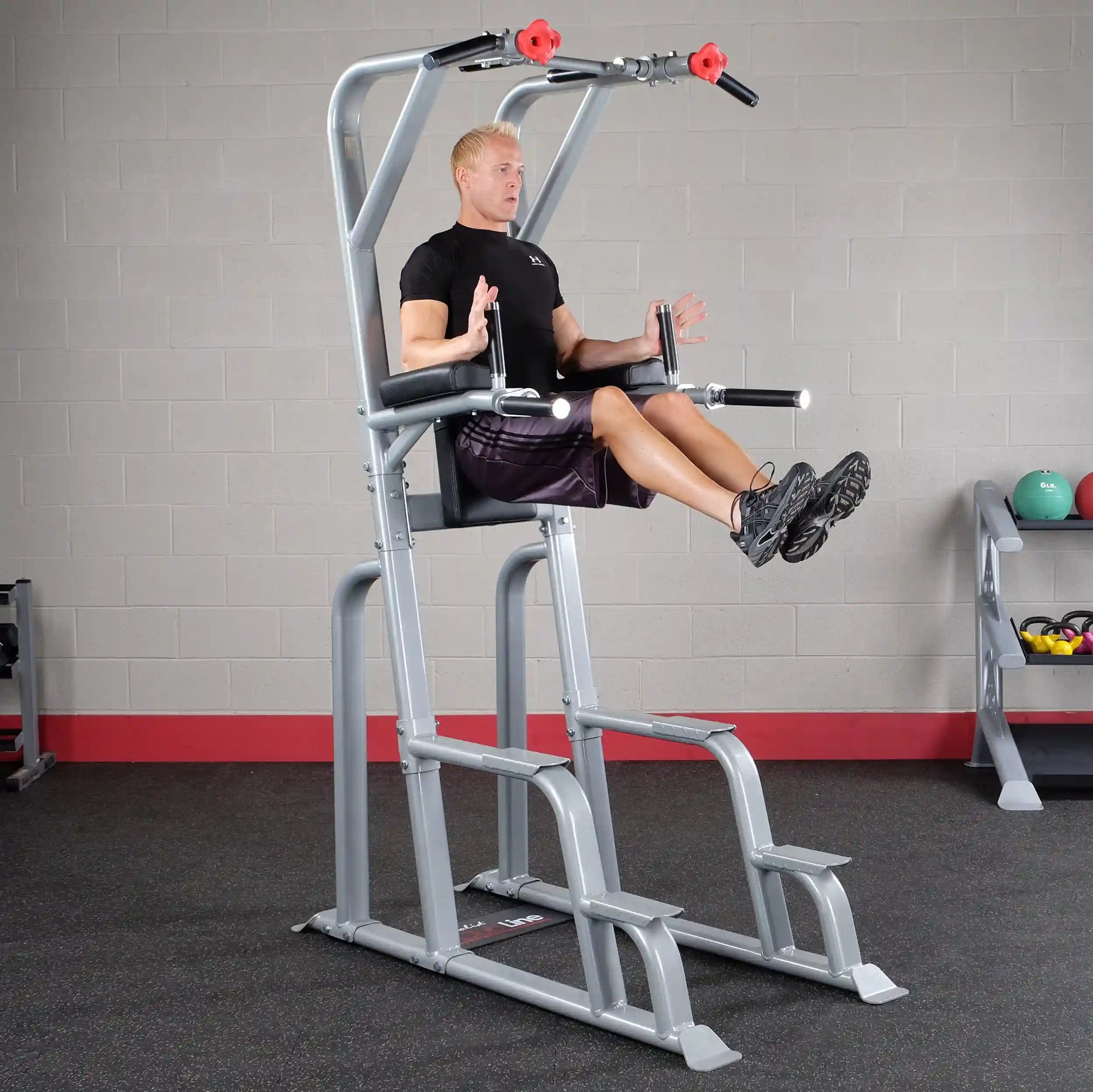 A person demonstrating an exercise on the Body-Solid Pro Clubline Vertical Knee Raise SVKR1000, focusing on core strength, in a gym setting with fitness equipment in the background.
