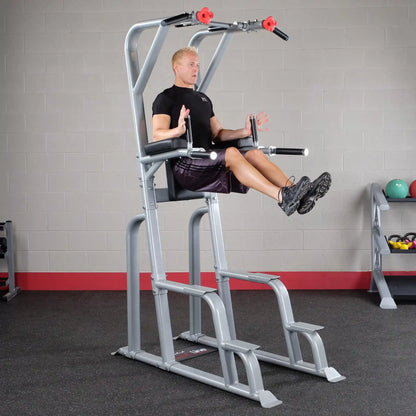 A person demonstrating an exercise on the Body-Solid Pro Clubline Vertical Knee Raise SVKR1000, focusing on core strength, in a gym setting with fitness equipment in the background.
