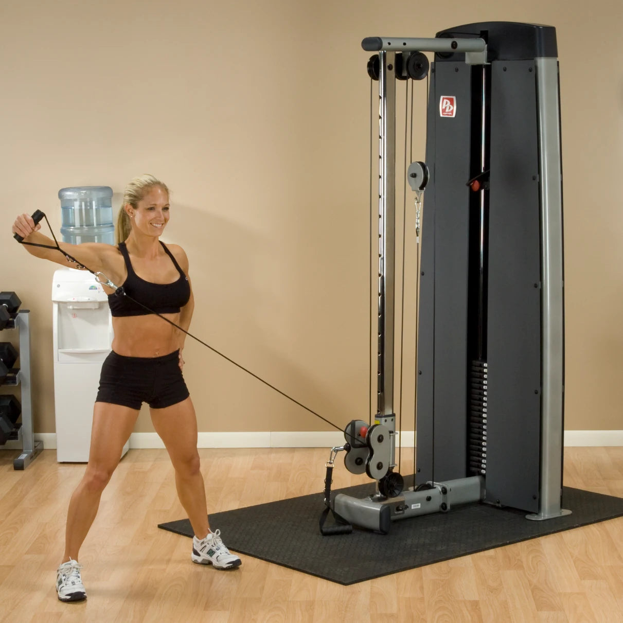 A woman performing an exercise using the Body-Solid Pro Dual Cable Column Machine DPCCSF in a gym setting.