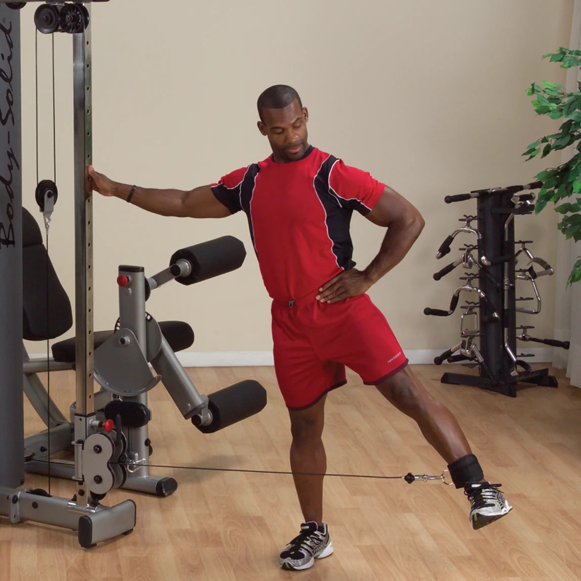 A person exercising with the Body-Solid Pro Dual Cable Column Machine DPCCSF, performing a leg lift while holding onto the machine for support.