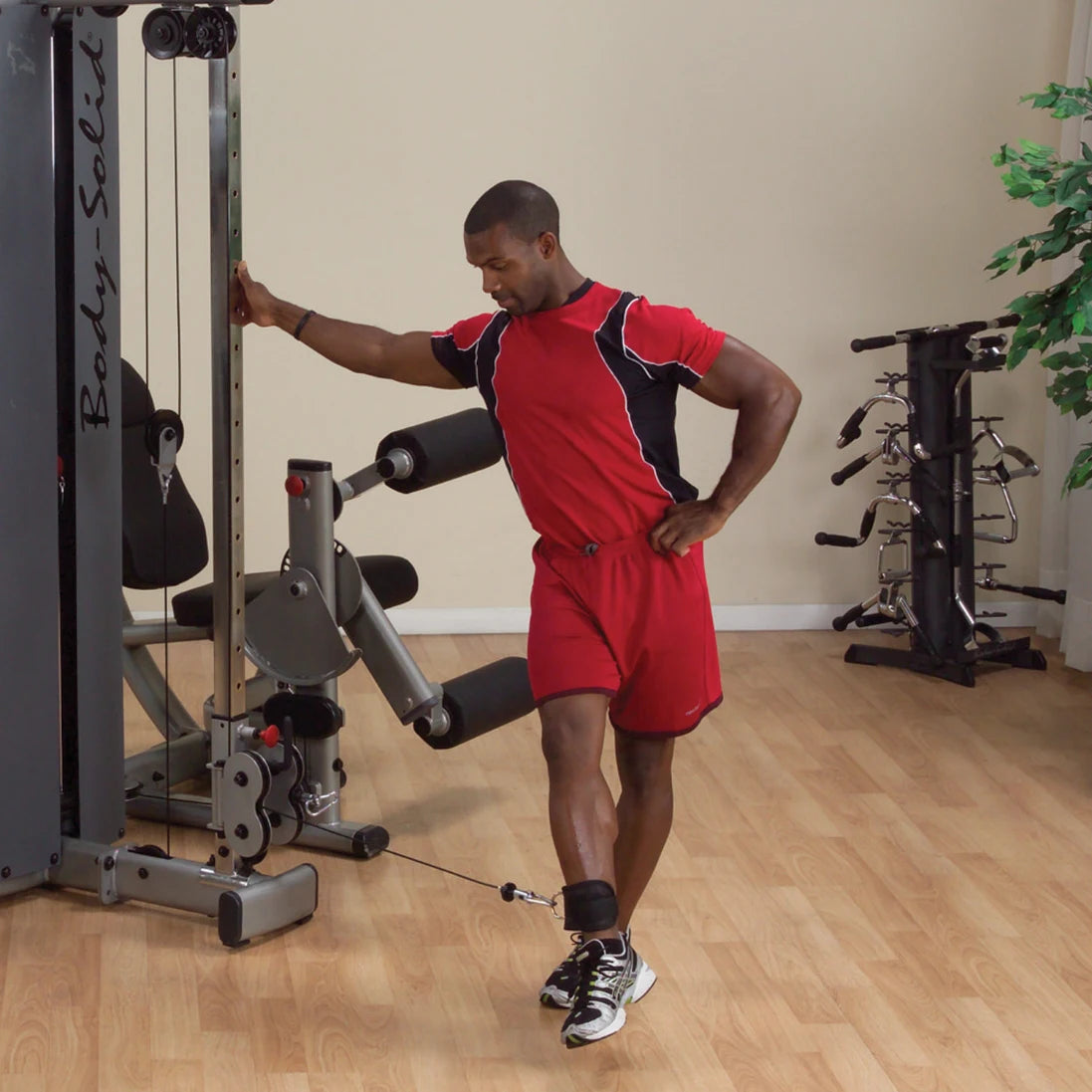 Man performing an exercise using the Body-Solid Pro Dual Cable Column Machine DPCCSF, with one leg extended and a cable attached to his ankle.