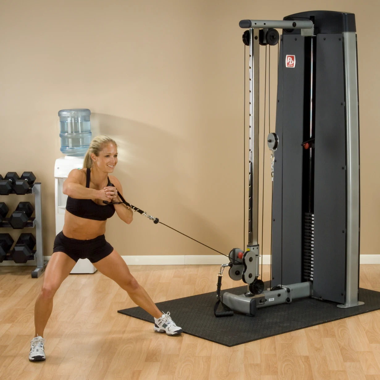 A woman exercising with the Body-Solid Pro Dual Cable Column Machine DPCCSF in a fitness studio, demonstrating a cable pull exercise.