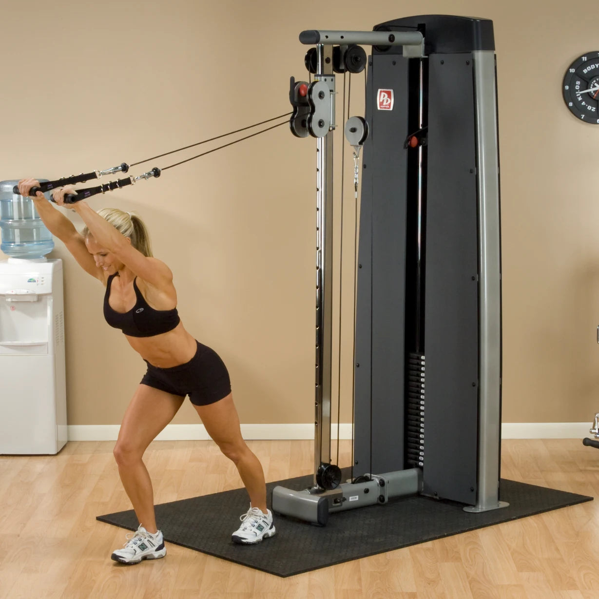 A woman performs an exercise using the Body-Solid Pro Dual Cable Column Machine DPCCSF in a gym setting, showcasing her strength and fitness.