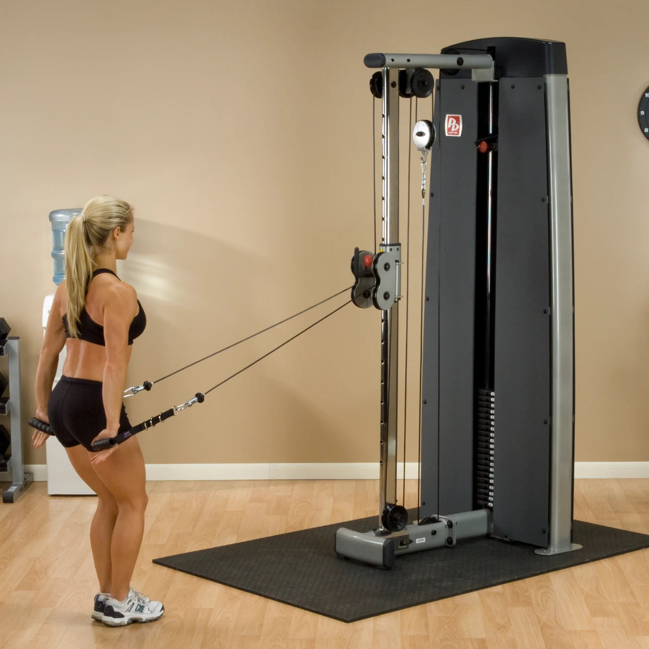 A woman performing an exercise using the Body-Solid Pro Dual Cable Column Machine DPCCSF in a gym setting.