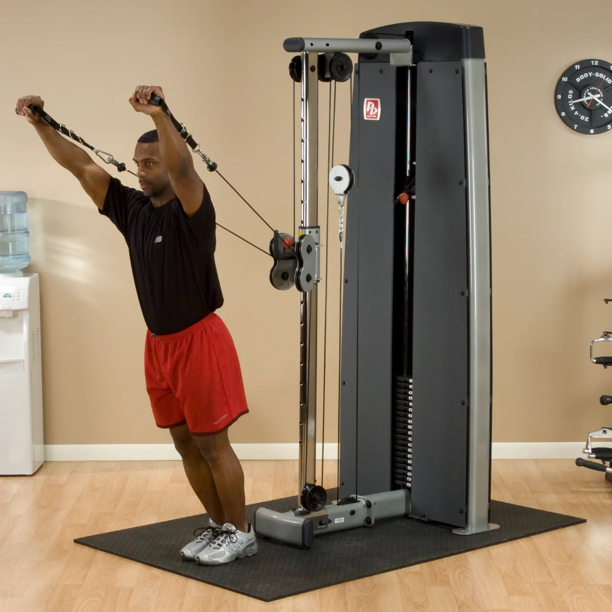 A man performing an exercise using the Body-Solid Pro Dual Cable Column Machine DPCCSF, with cables extended overhead in a fitness studio setting.