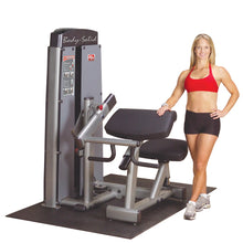 A fitness model standing next to the Body-Solid Pro Dual Bicep & Tricep Machine DBTCSF, showcasing its design and features in a gym setting.