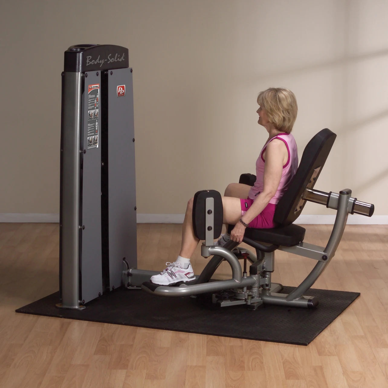 A woman using the Body-Solid Pro Dual Inner & Outer Thigh Machine DIOTSF in a fitness studio, seated with her legs positioned on the machine.
