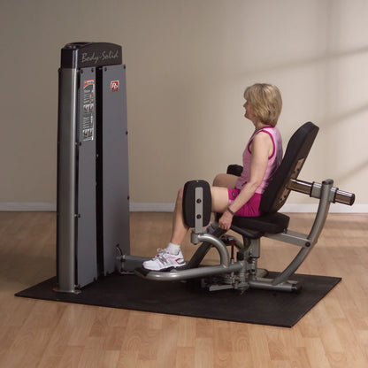 A woman using the Body-Solid Pro Dual Inner & Outer Thigh Machine DIOTSF in a fitness studio, seated with her legs positioned on the machine.