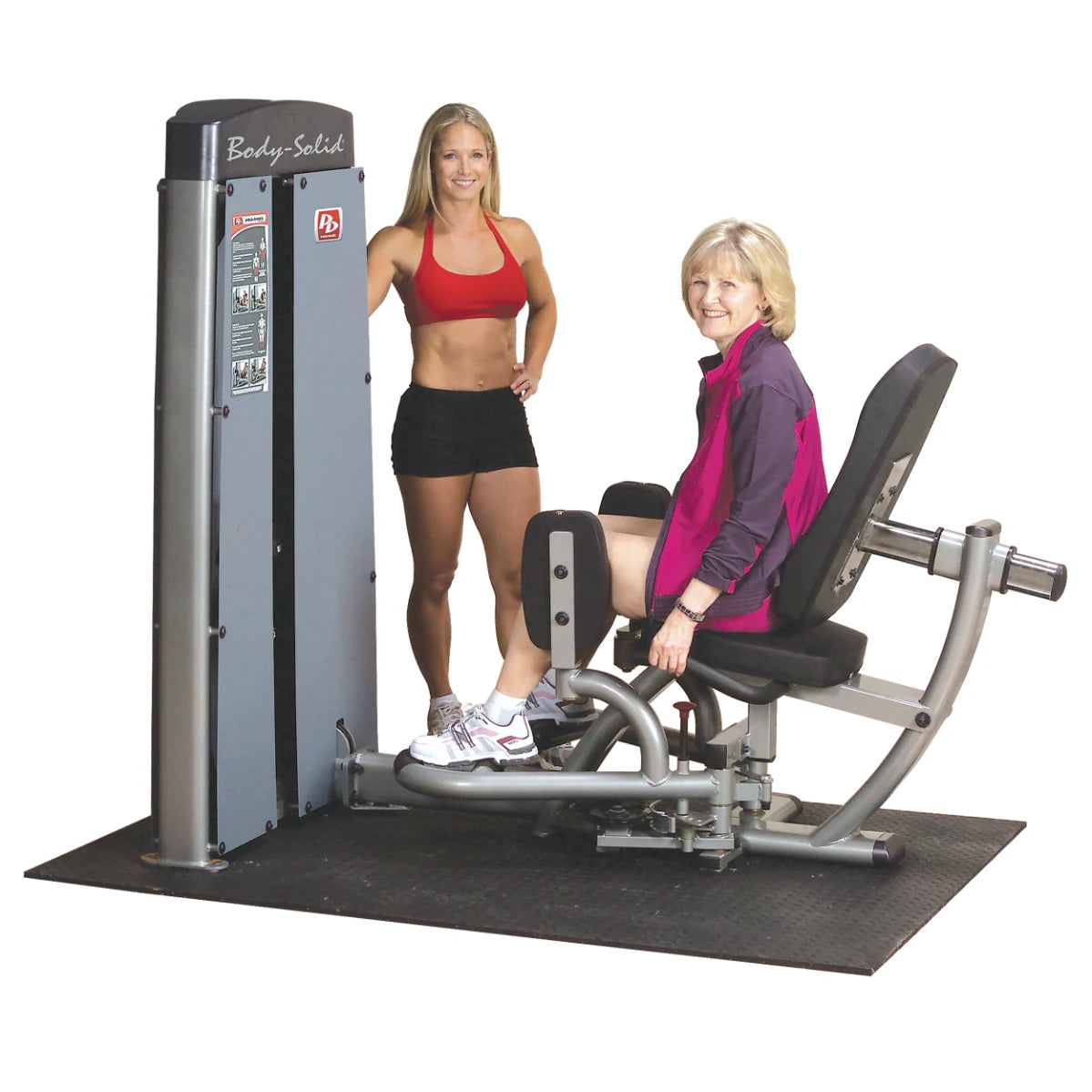 Two women using the Body-Solid Pro Dual Inner & Outer Thigh Machine DIOTSF in a gym setting, one demonstrating the machine while the other is seated and exercising.