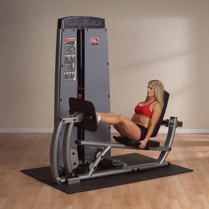 A woman using the Body-Solid Pro Dual Leg & Calf Press Machine DCLPSF in a fitness studio, demonstrating a leg press exercise.