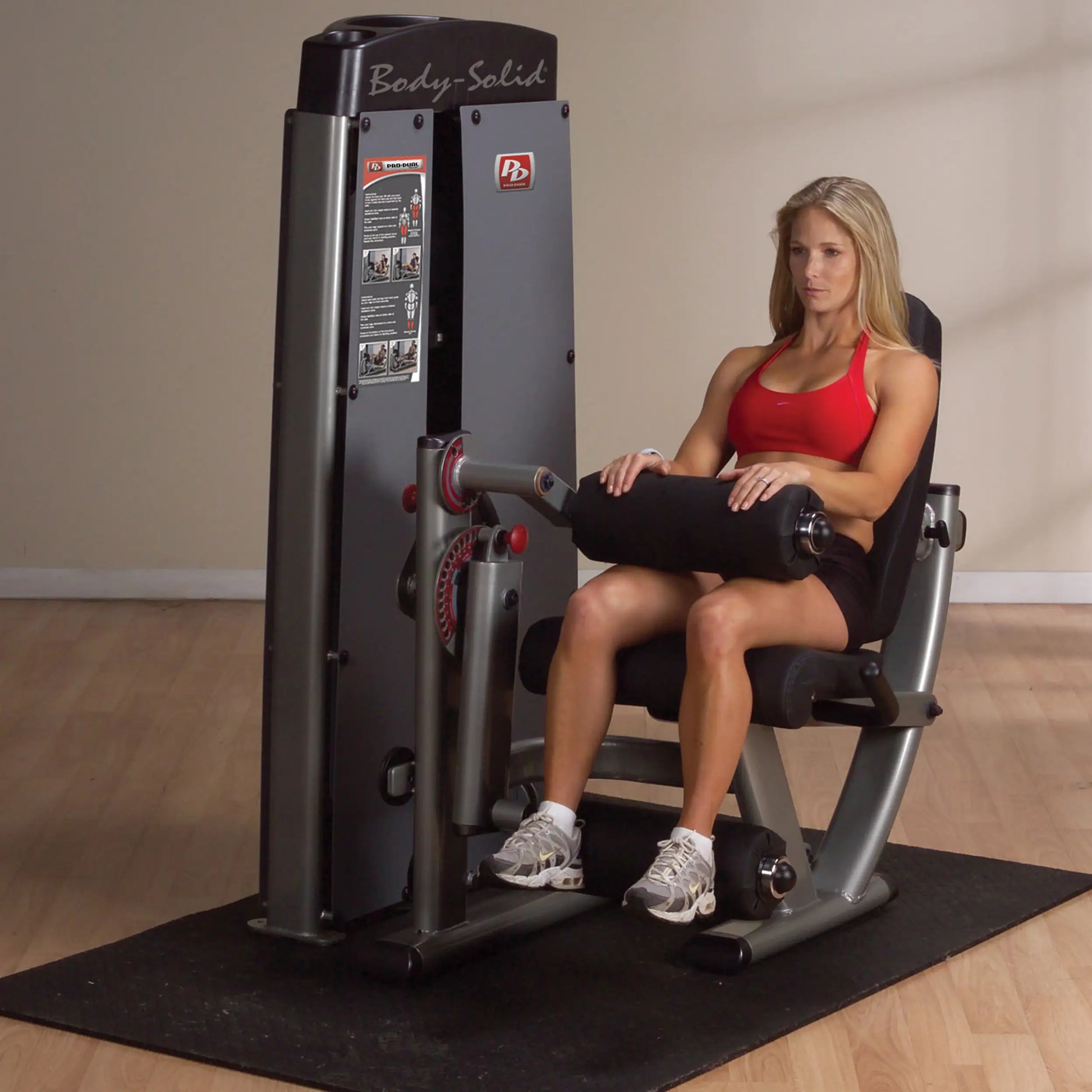 A woman using the Body-Solid Pro Dual Leg Extension & Curl Machine DLECSF in a gym setting, demonstrating leg exercises.