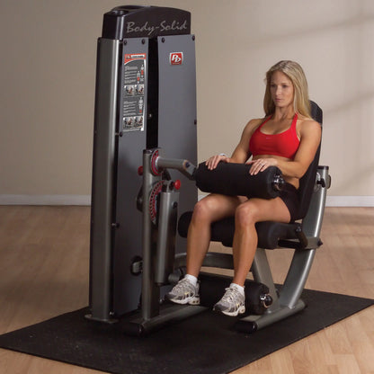 A woman using the Body-Solid Pro Dual Leg Extension & Curl Machine DLECSF in a gym setting, demonstrating leg exercises.