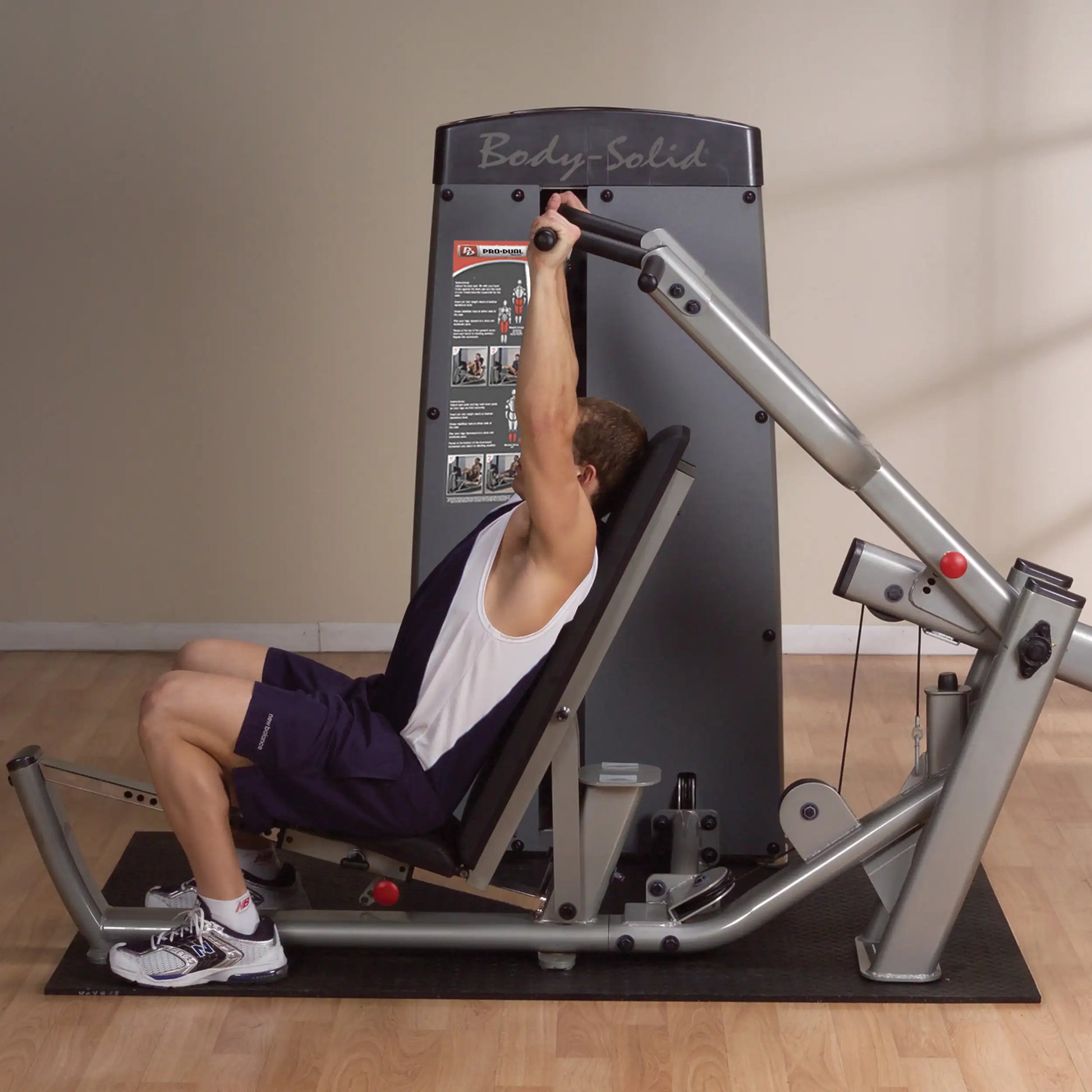 A person using the Body-Solid Pro Dual Multi-Press Machine DPRSSF, performing an overhead press exercise on a padded bench in a gym setting.
