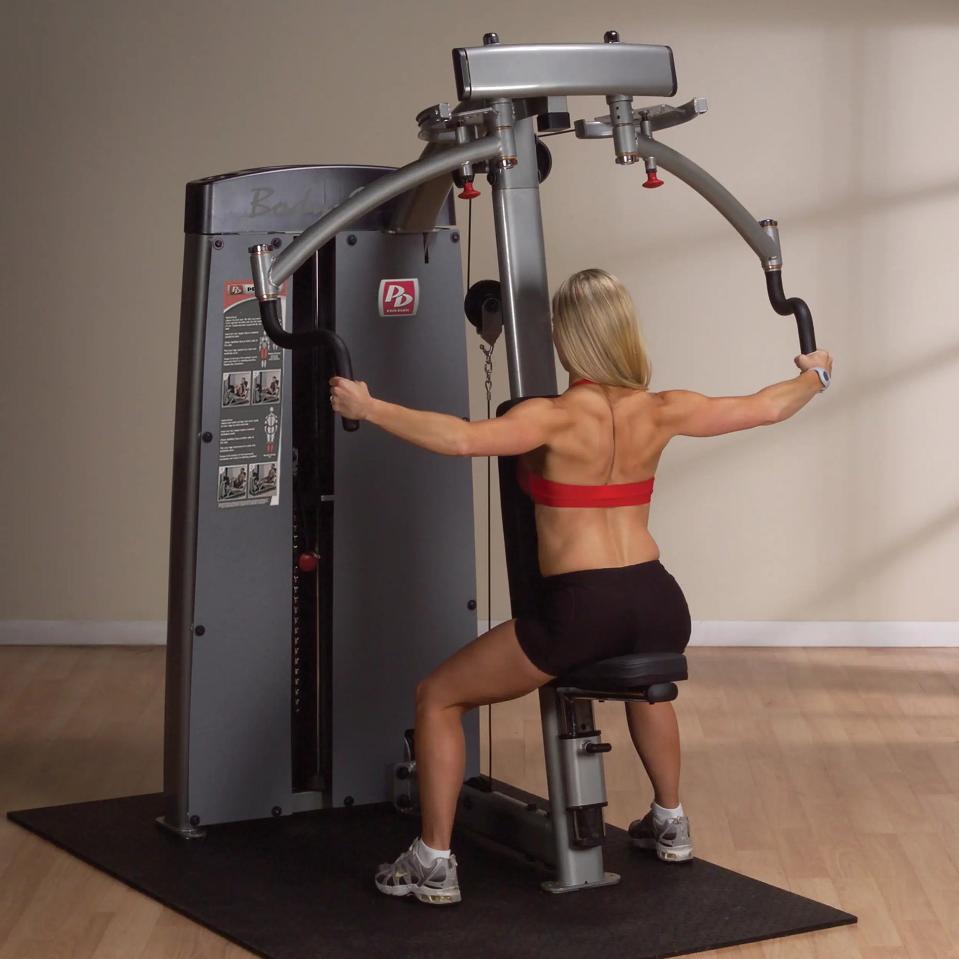 A woman using the Body-Solid Pro Dual Pec & Rear Delt Machine DPECSF in a gym setting, performing an exercise targeting the chest and rear deltoids, with a focus on her upper body strength.