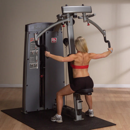 A woman using the Body-Solid Pro Dual Pec & Rear Delt Machine DPECSF in a gym setting, performing an exercise targeting the chest and rear deltoids, with a focus on her upper body strength.