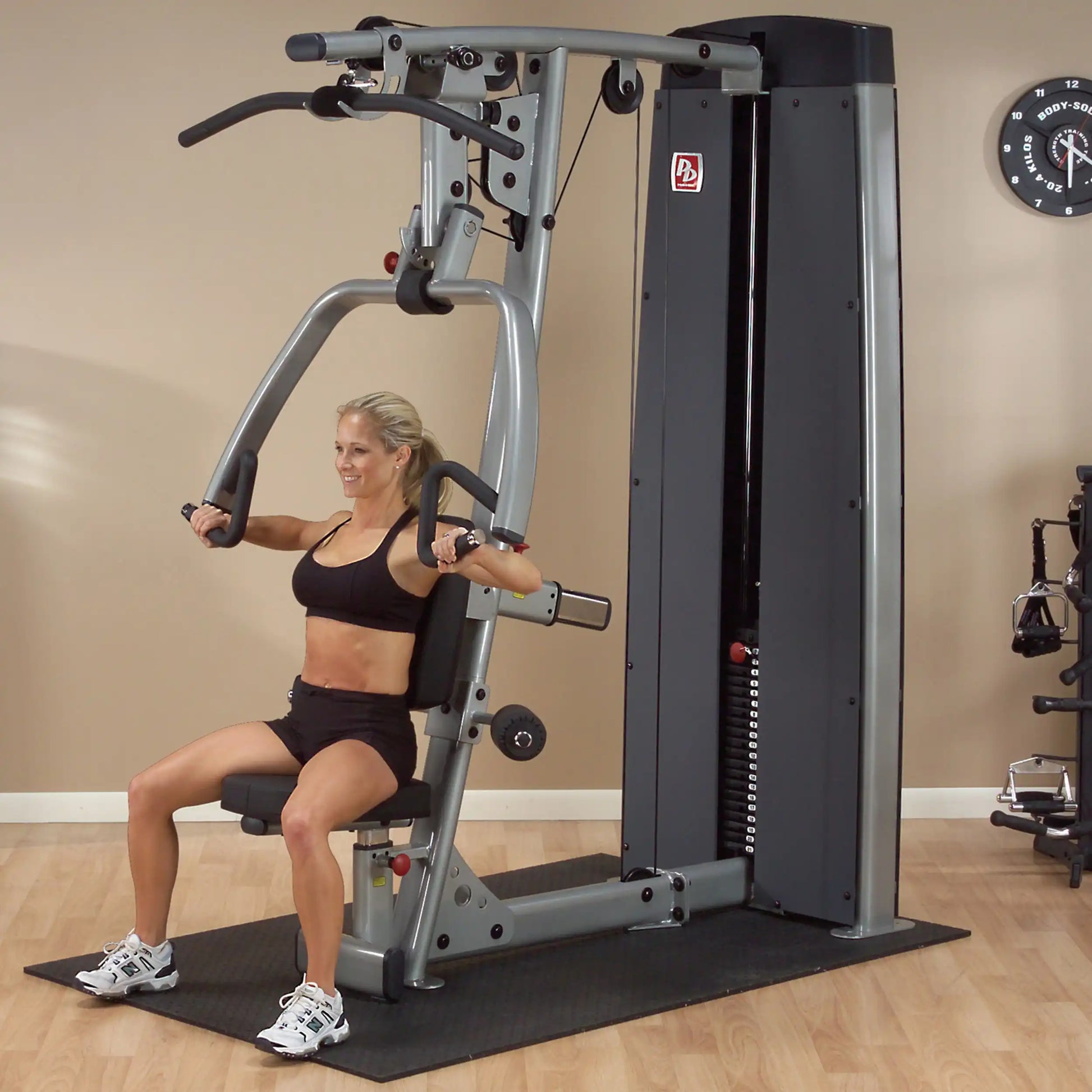 A woman using the Body-Solid Pro Dual Vertical Press & Lat Machine DPLSSF in a fitness studio, demonstrating an exercise while seated.