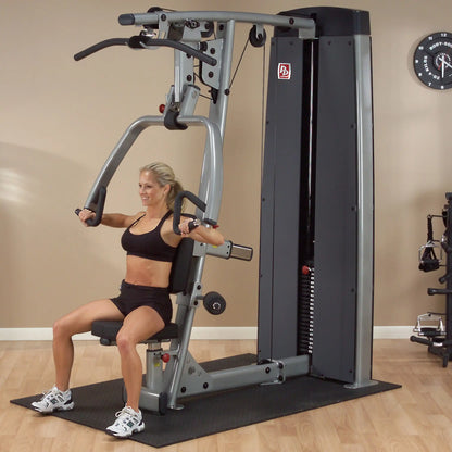 A woman using the Body-Solid Pro Dual Vertical Press & Lat Machine DPLSSF in a fitness studio, demonstrating an exercise while seated.