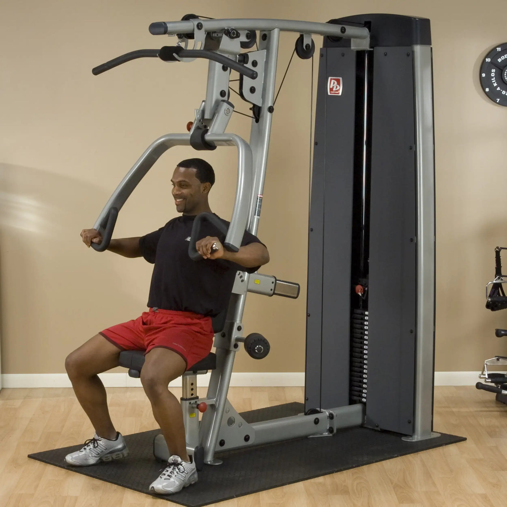 A man using the Body-Solid Pro Dual Vertical Press & Lat Machine DPLSSF in a gym setting, smiling while performing an exercise.