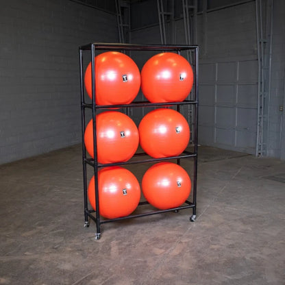 Six orange exercise balls on a black rack in a gym storage room.