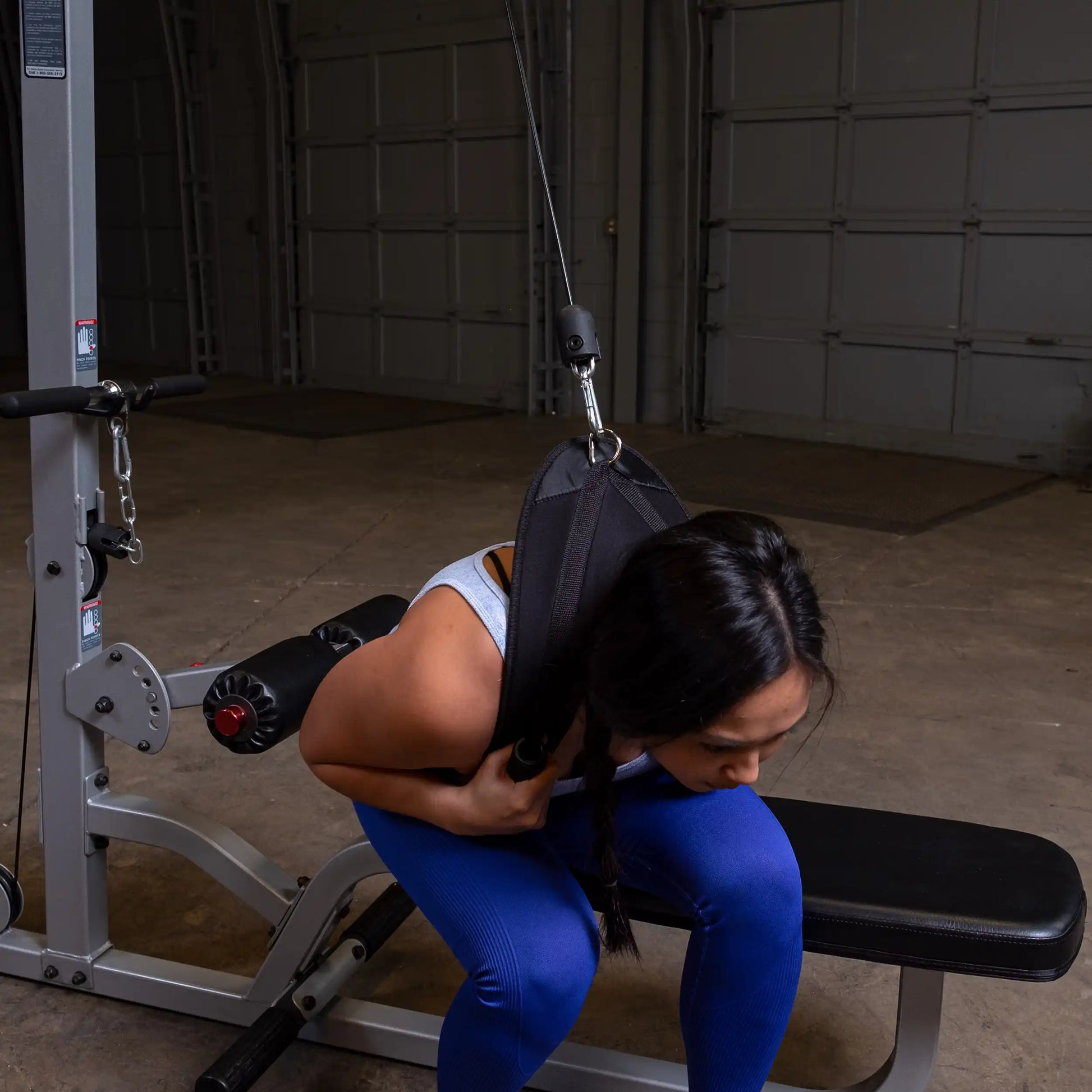 Woman using EliteFTS reverse hyper machine with black strap in gym.