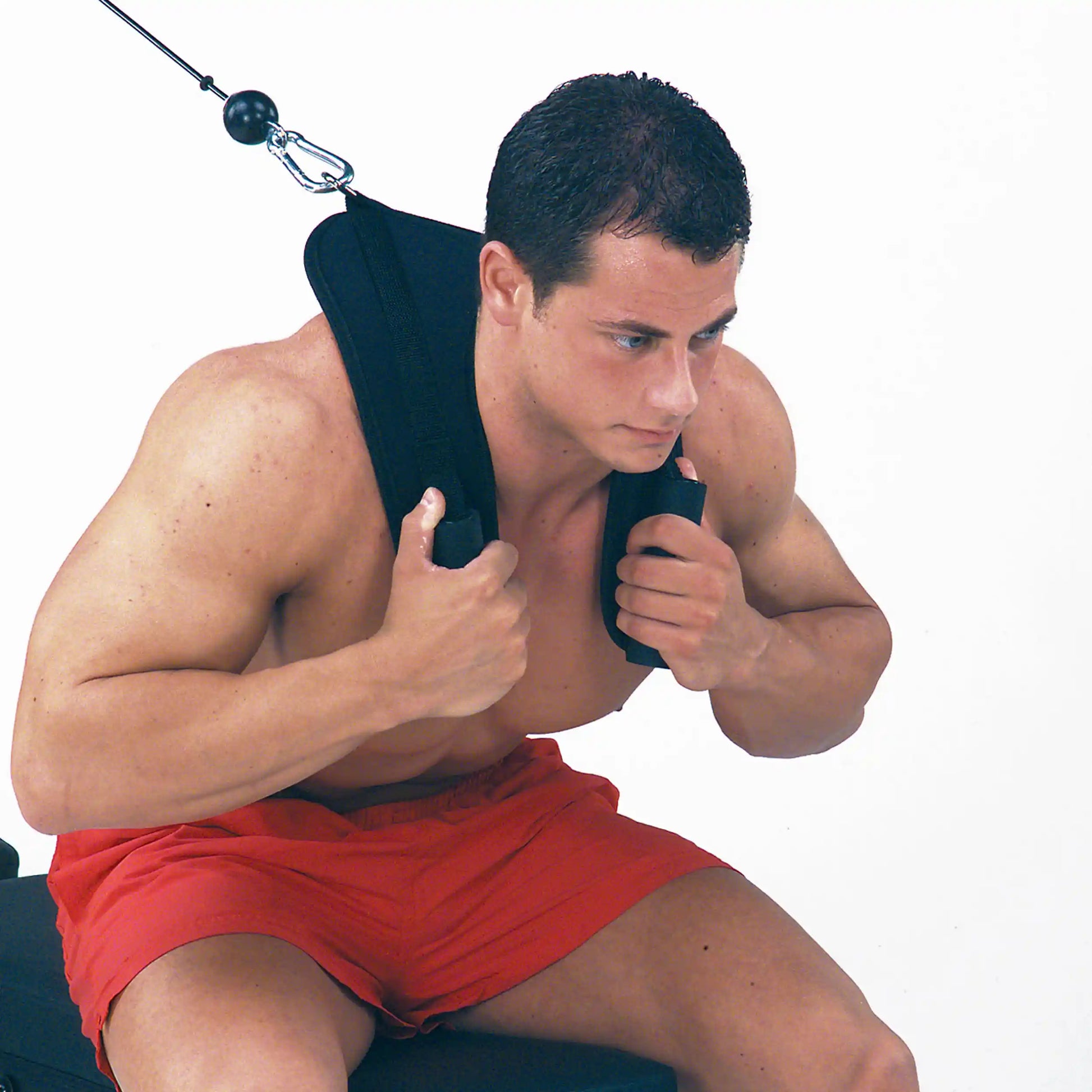 Man using neck harness for strength training in red shorts.