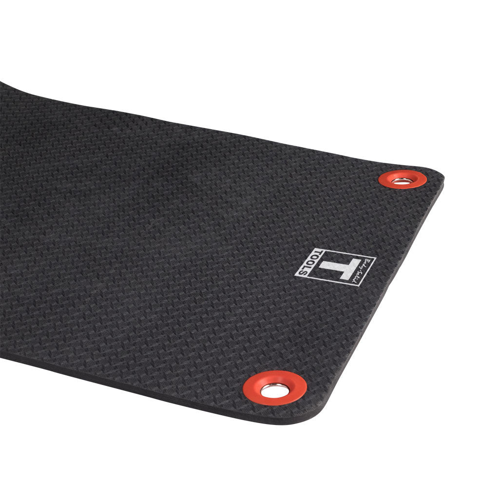 Black foam exercise mat with textured surface and red circular anchor grommets at corners. White brand logo visible on mat.