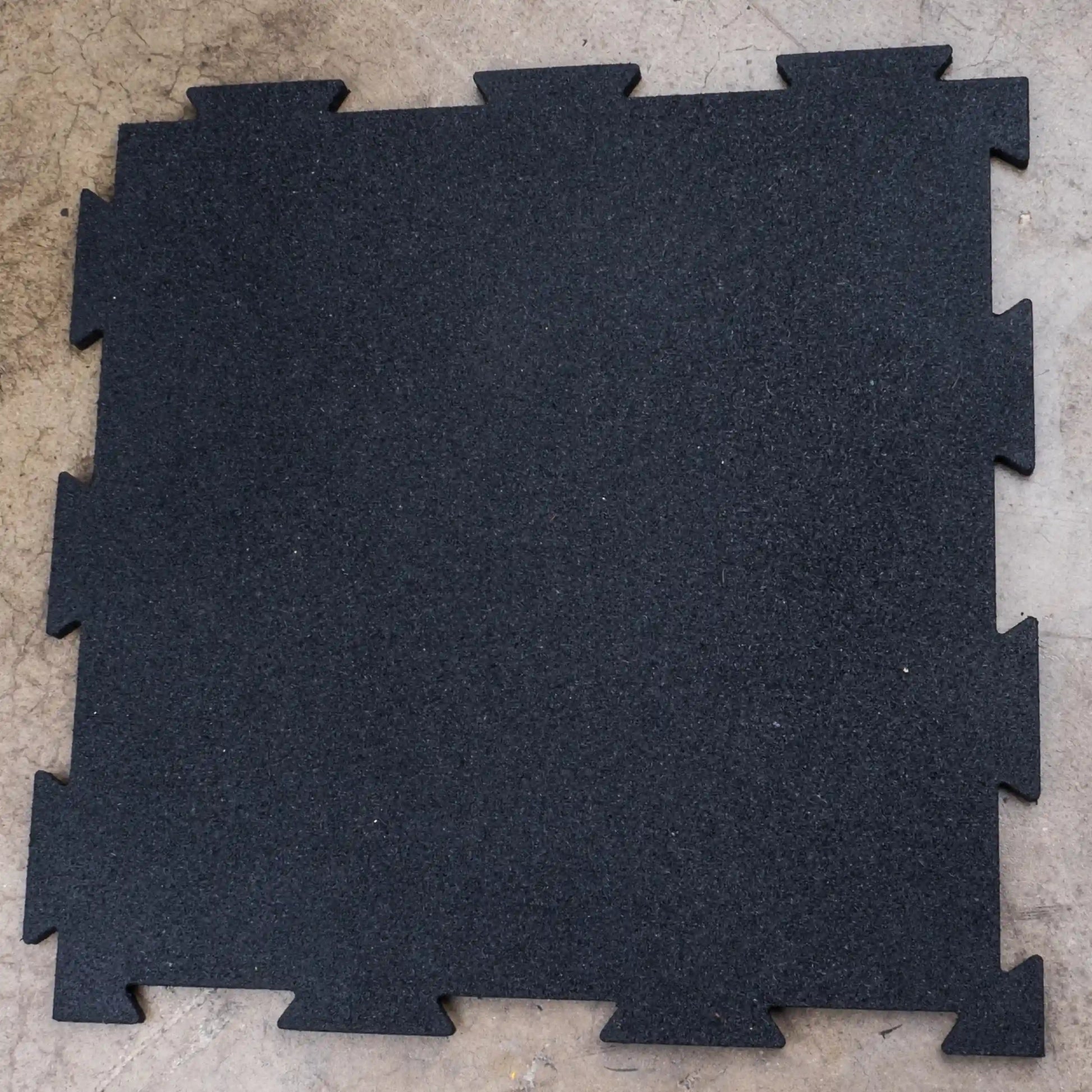 Black rubber gym flooring tile with interlocking edges on concrete floor.