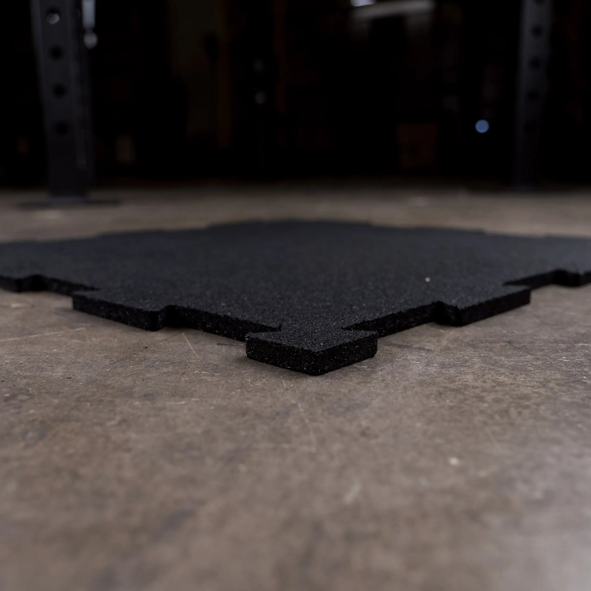 Black interlocking rubber flooring tile on a concrete gym floor.