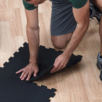 Man assembling black foam puzzle exercise mat on wooden floor.
