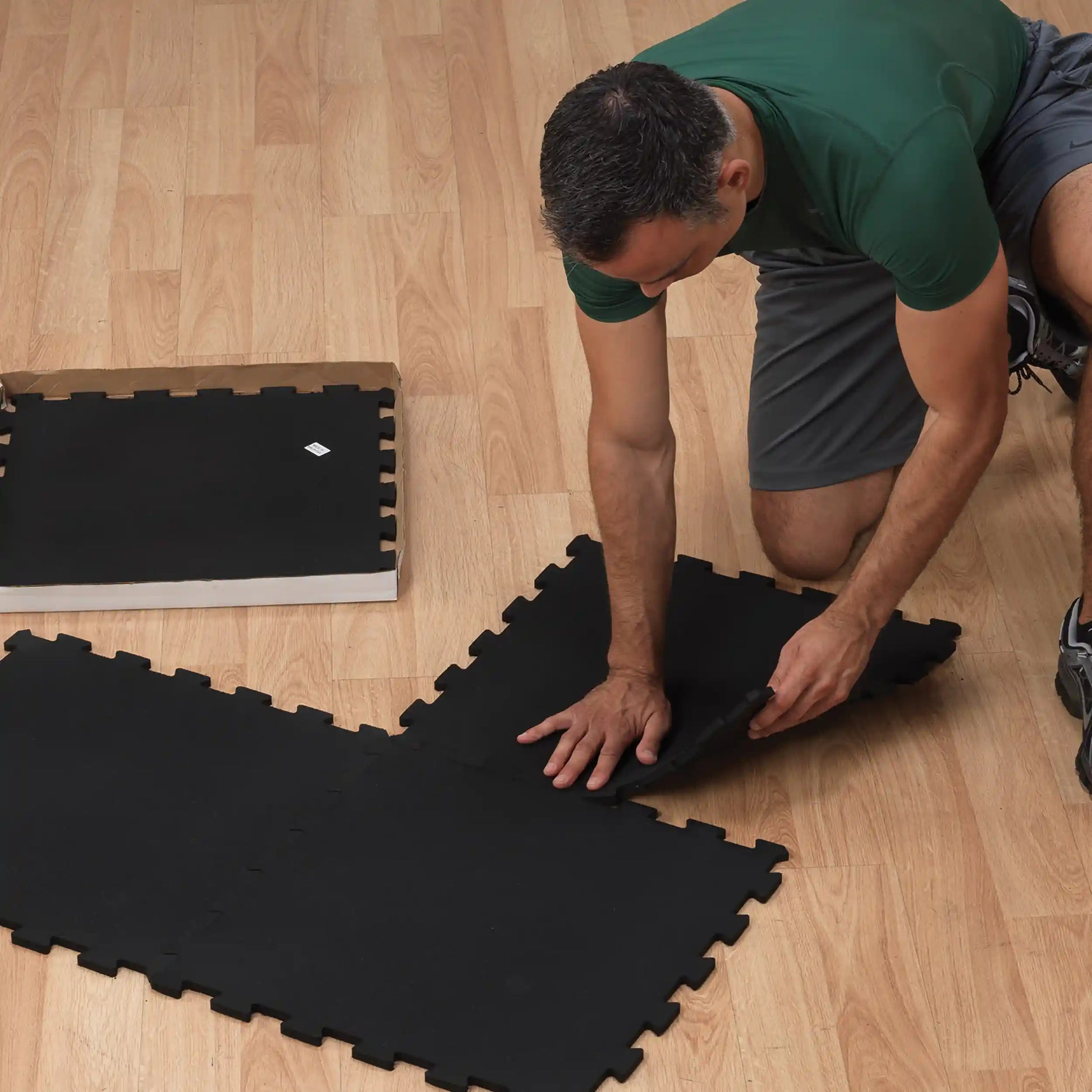 Man installing black foam floor mats on wooden surface.